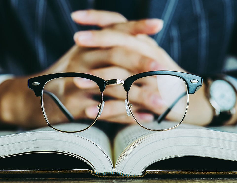 An image of a person with their fingers interlinked and their glasses are sitting on an open book. This image is used as a banner for the MetaPerformance Business Analysis as a Service (BAaaS.) service page.